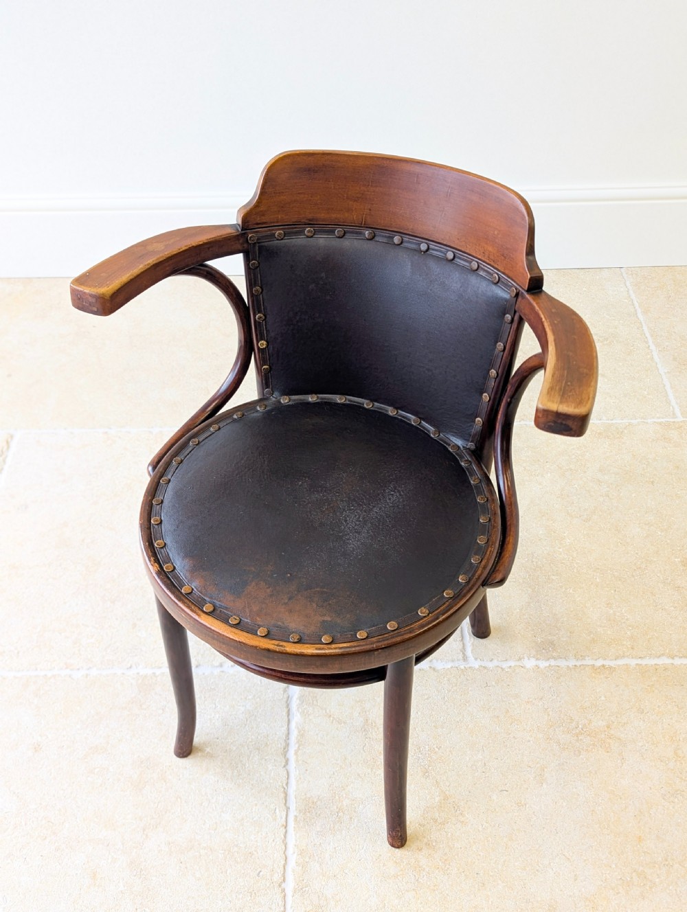 An antique Edwardian bentwood armchair featuring dark brown steam-bent beech wood, sweeping armrests, and a black leather studded seat and backrest. View II
