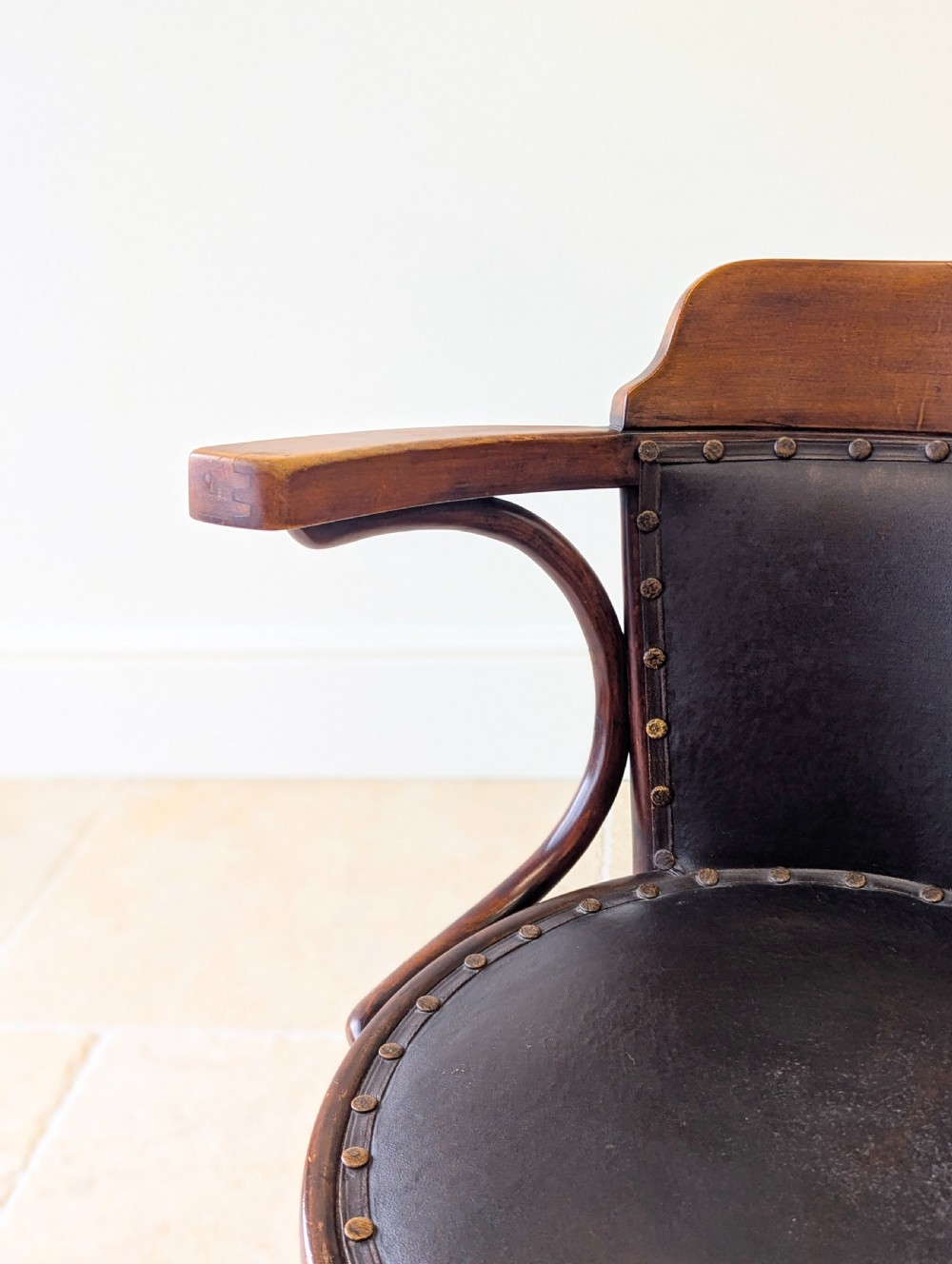 An antique Edwardian bentwood armchair featuring dark brown steam-bent beech wood, sweeping armrests, and a black leather studded seat and backrest. View IV