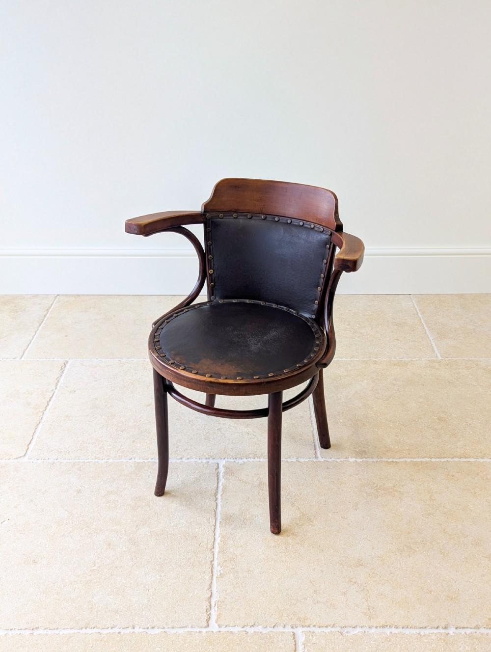 An antique Edwardian bentwood armchair featuring dark brown steam-bent beech wood, sweeping armrests, and a black leather studded seat and backrest. View V