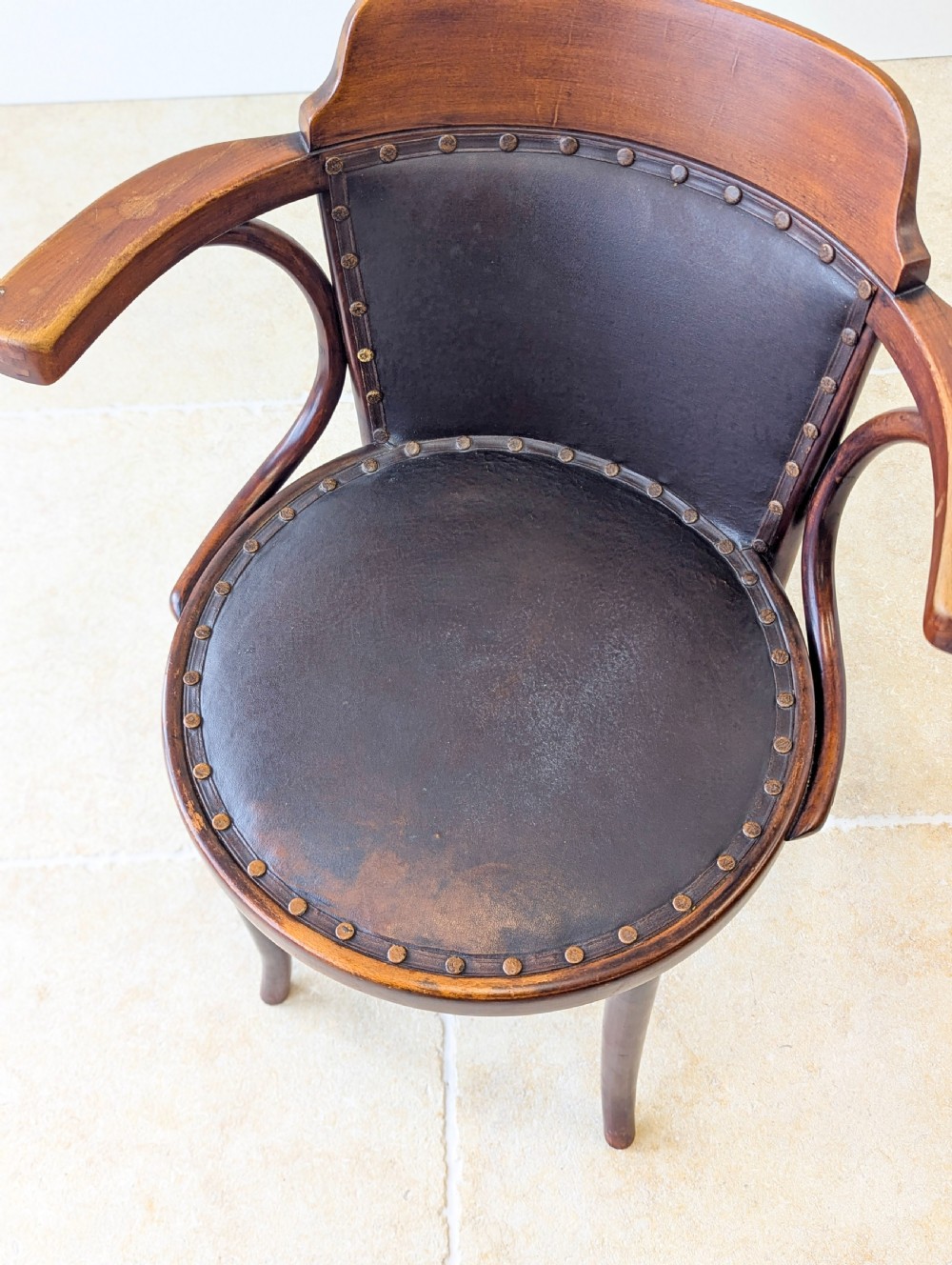 An antique Edwardian bentwood armchair featuring dark brown steam-bent beech wood, sweeping armrests, and a black leather studded seat and backrest. View IX