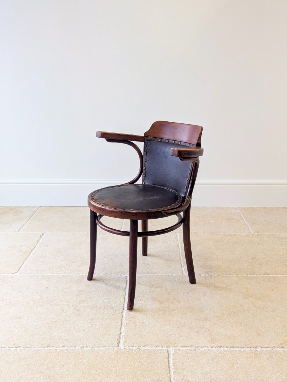 An antique Edwardian bentwood armchair featuring dark brown steam-bent beech wood, sweeping armrests, and a black leather studded seat and backrest. View X