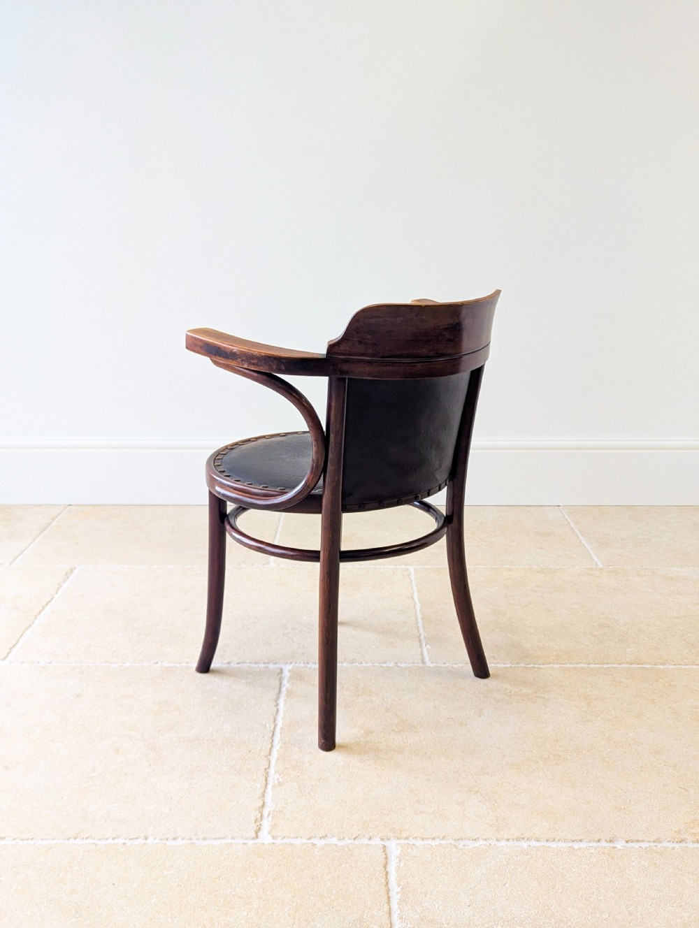 An antique Edwardian bentwood armchair featuring dark brown steam-bent beech wood, sweeping armrests, and a black leather studded seat and backrest. View XIV