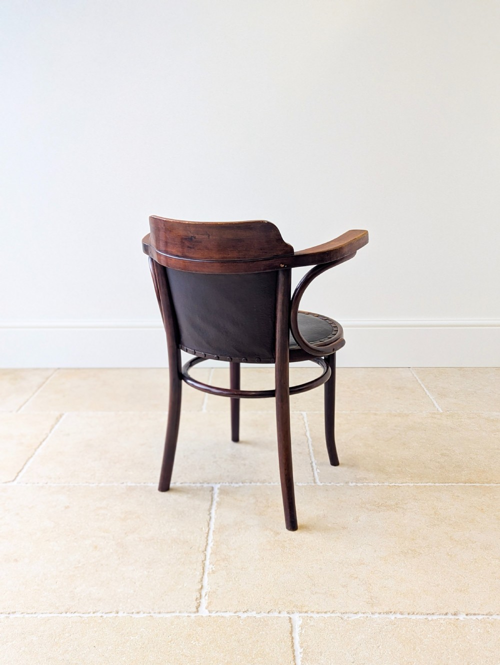 An antique Edwardian bentwood armchair featuring dark brown steam-bent beech wood, sweeping armrests, and a black leather studded seat and backrest. View XV