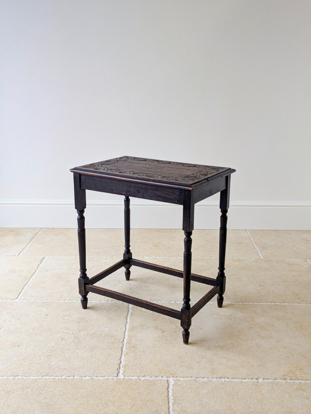 An Edwardian dark oak rectangular occasional table featuring a relief-carved foliate border on the top, slender turned legs, and lower perimeter stretchers.