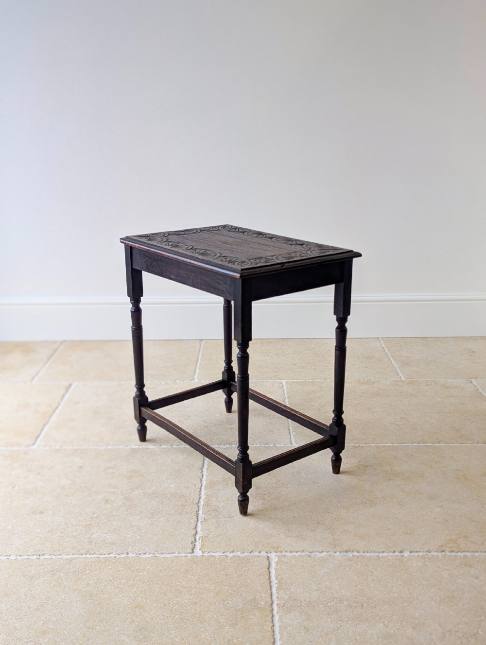 An Edwardian dark oak rectangular occasional table featuring a relief-carved foliate border on the top, slender turned legs, and lower perimeter stretchers. View V