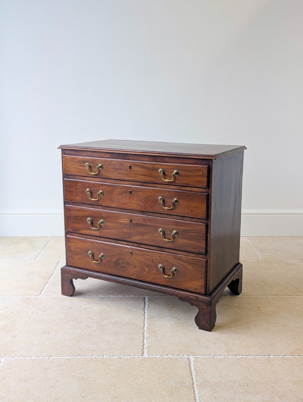 An 18th-century George III mahogany chest of drawers featuring four graduated drawers with brass swan-neck handles and bracket feet.