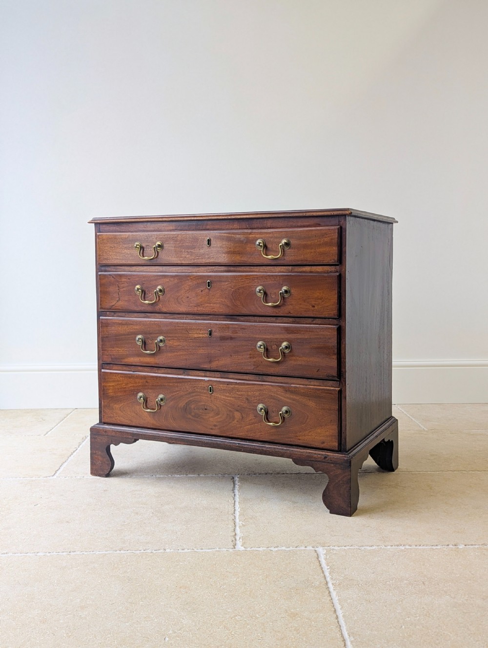 An 18th-century George III mahogany chest of drawers featuring four graduated drawers with brass swan-neck handles and bracket feet. View IV
