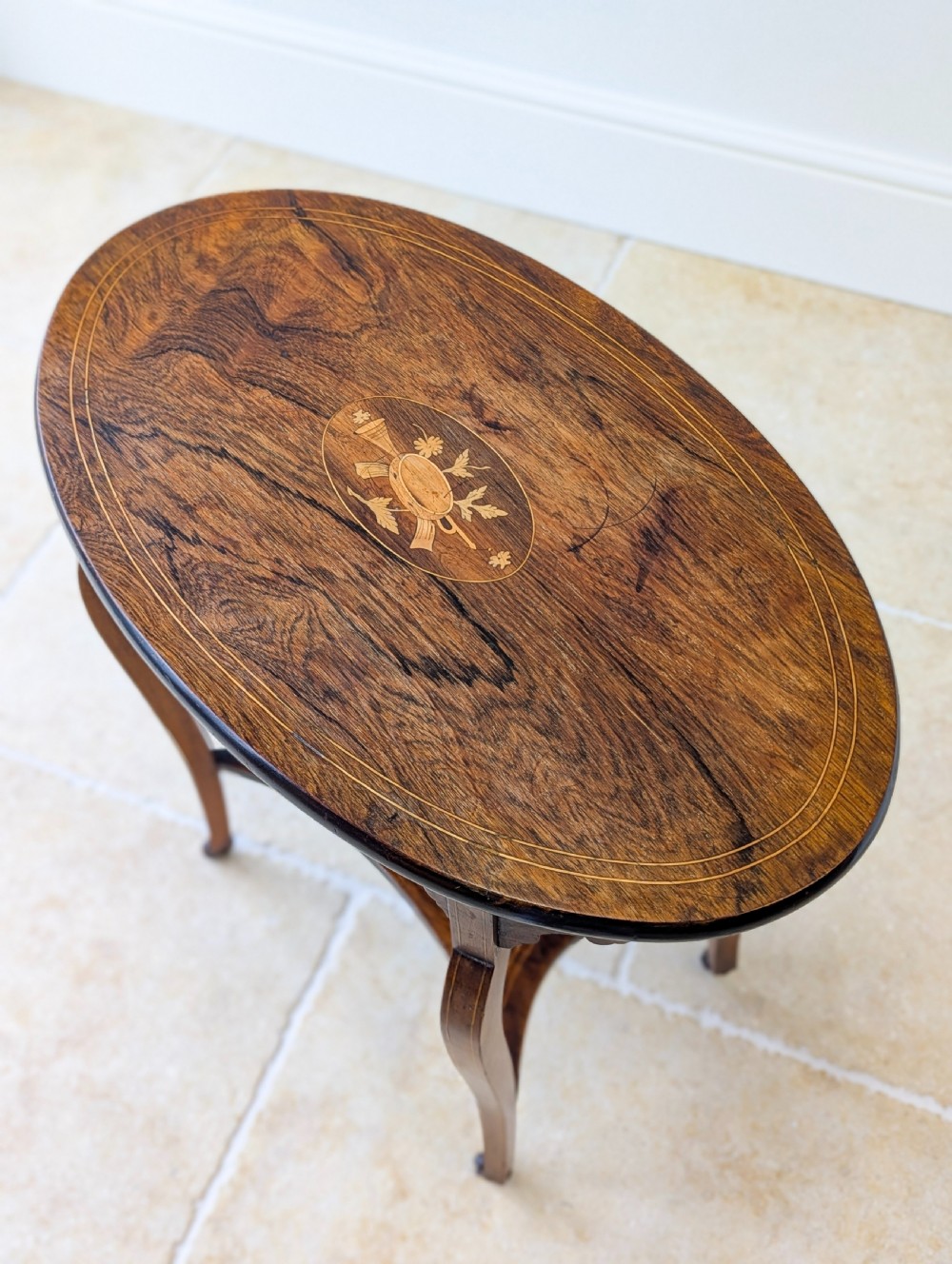 An Edwardian rosewood oval occasional table with marquetry inlay on the tabletop, slender cabriole legs, a shaped lower shelf, and brass castors. View II