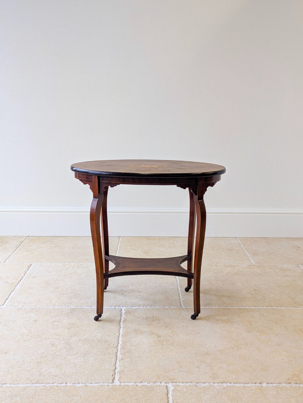 An Edwardian rosewood oval occasional table with marquetry inlay on the tabletop, slender cabriole legs, a shaped lower shelf, and brass castors. View III