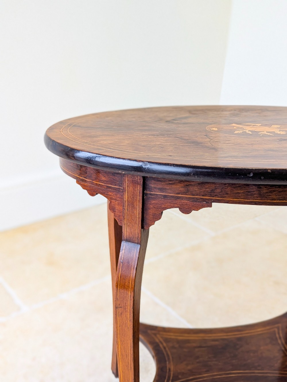 An Edwardian rosewood oval occasional table with marquetry inlay on the tabletop, slender cabriole legs, a shaped lower shelf, and brass castors. View IV
