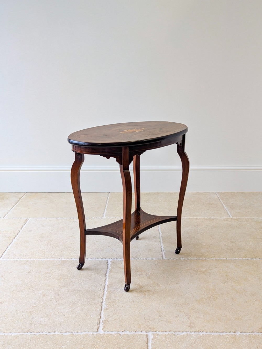An Edwardian rosewood oval occasional table with marquetry inlay on the tabletop, slender cabriole legs, a shaped lower shelf, and brass castors. View VII