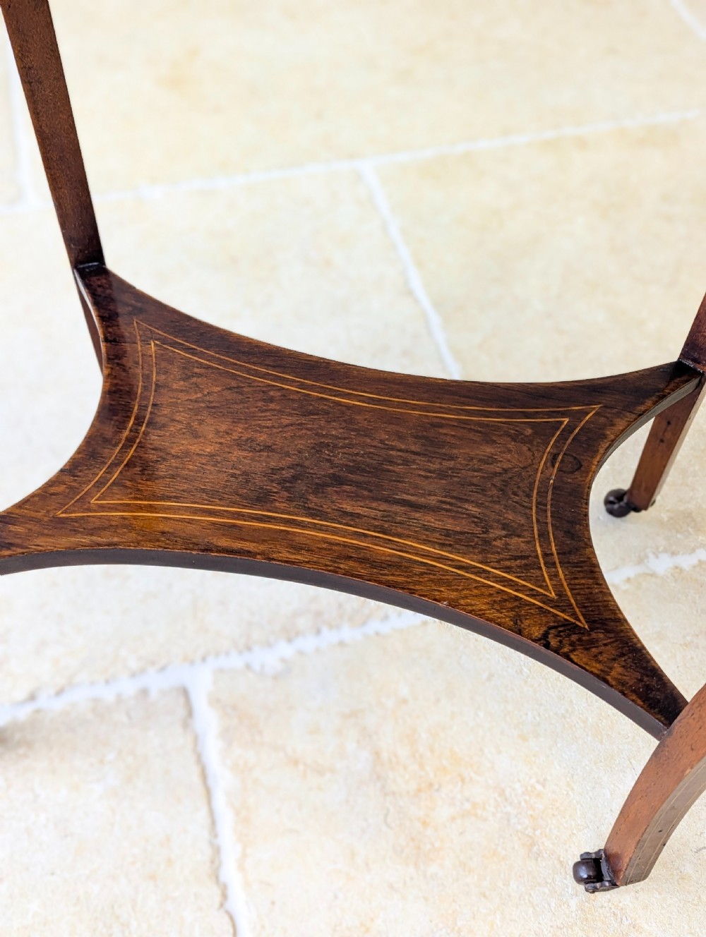 An Edwardian rosewood oval occasional table with marquetry inlay on the tabletop, slender cabriole legs, a shaped lower shelf, and brass castors. View X