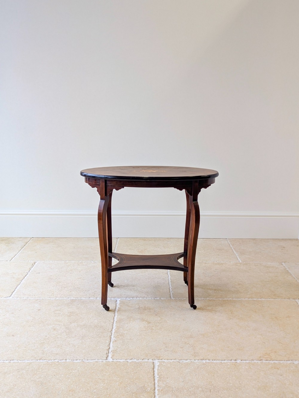 An Edwardian rosewood oval occasional table with marquetry inlay on the tabletop, slender cabriole legs, a shaped lower shelf, and brass castors. View XI