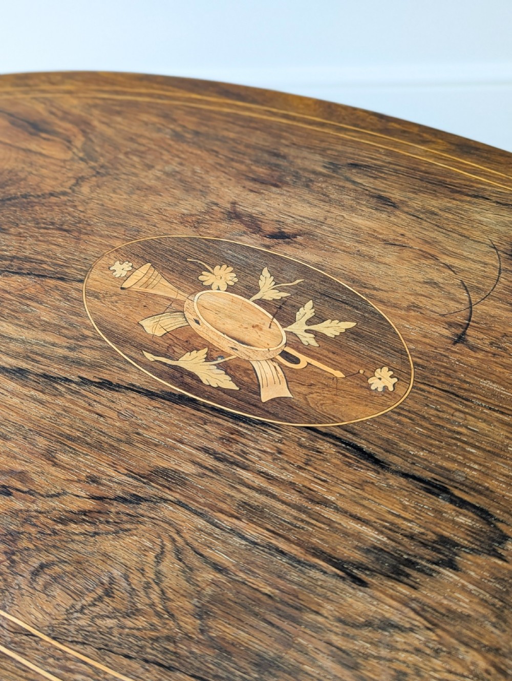 An Edwardian rosewood oval occasional table with marquetry inlay on the tabletop, slender cabriole legs, a shaped lower shelf, and brass castors. View XII