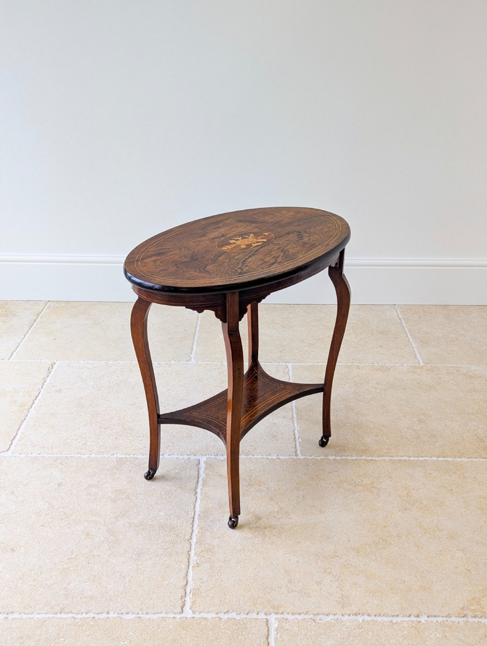 An Edwardian rosewood oval occasional table with marquetry inlay on the tabletop, slender cabriole legs, a shaped lower shelf, and brass castors. View XVIII
