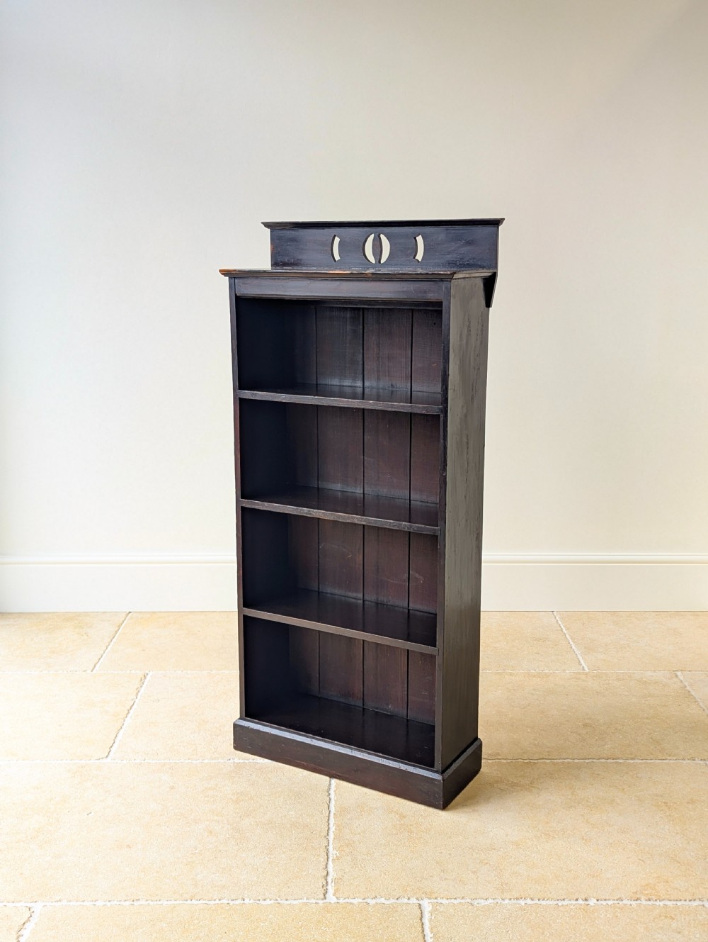 A tall, narrow late Victorian dark stained pine bookcase featuring four open shelves, a planked backboard, and a gallery top with pierced cutouts.