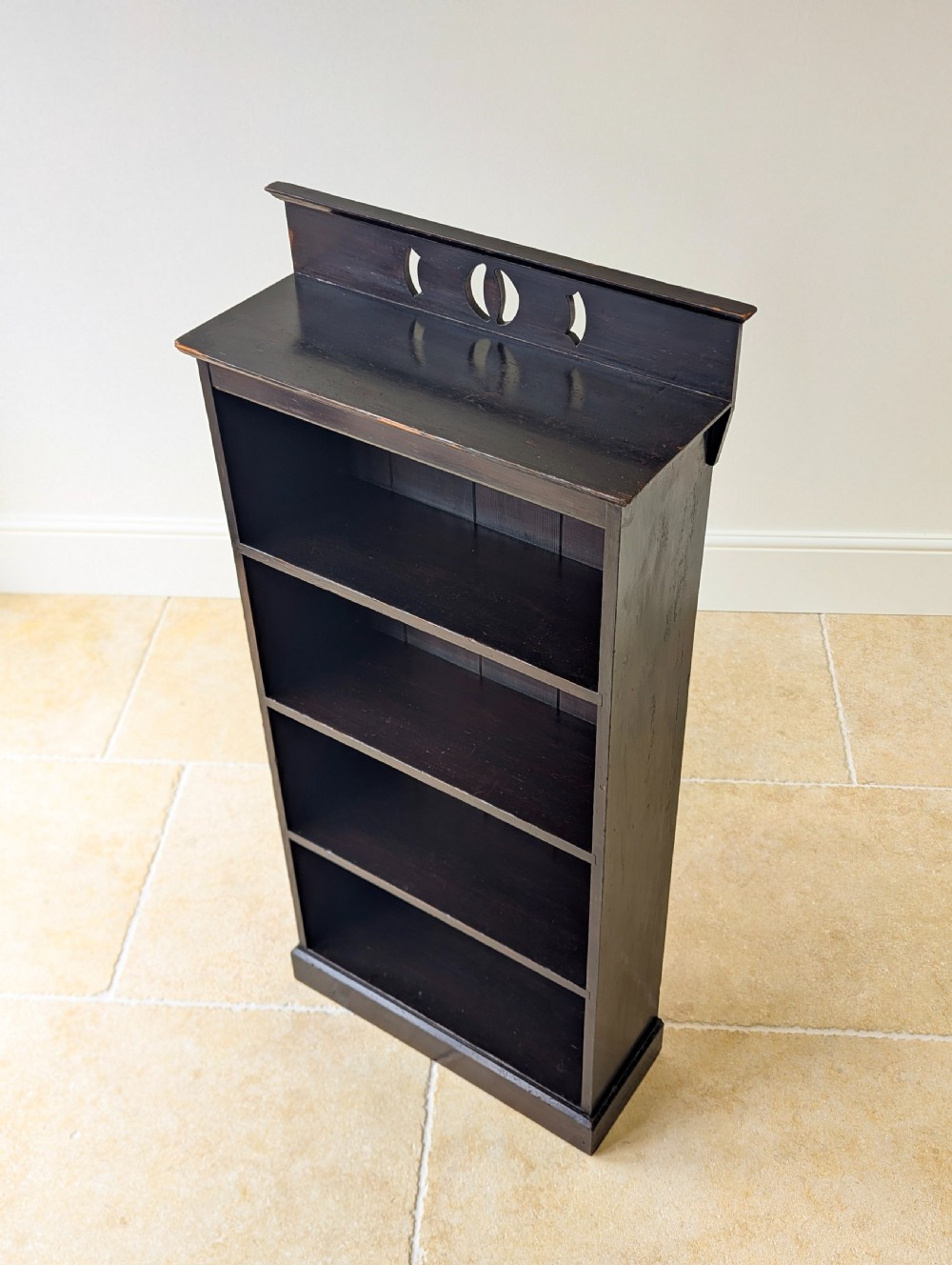 A tall, narrow late Victorian dark stained pine bookcase featuring four open shelves, a planked backboard, and a gallery top with pierced cutouts. View III