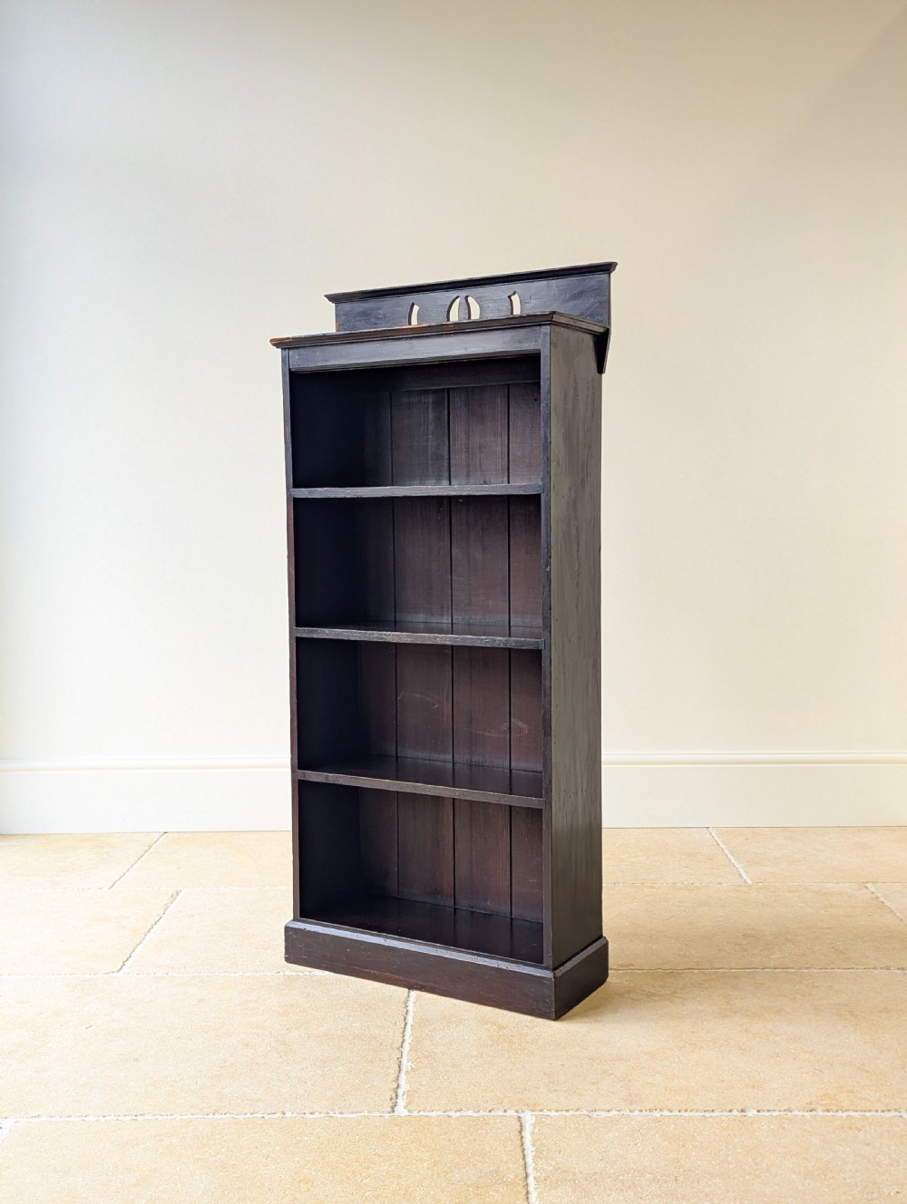 A tall, narrow late Victorian dark stained pine bookcase featuring four open shelves, a planked backboard, and a gallery top with pierced cutouts. View IV