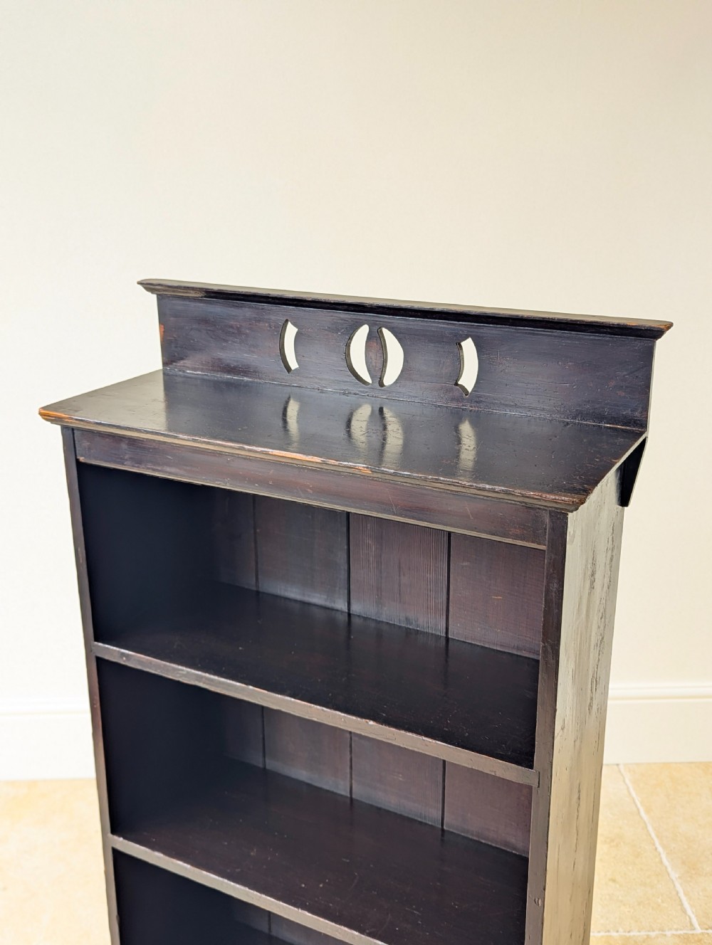 A tall, narrow late Victorian dark stained pine bookcase featuring four open shelves, a planked backboard, and a gallery top with pierced cutouts. View V