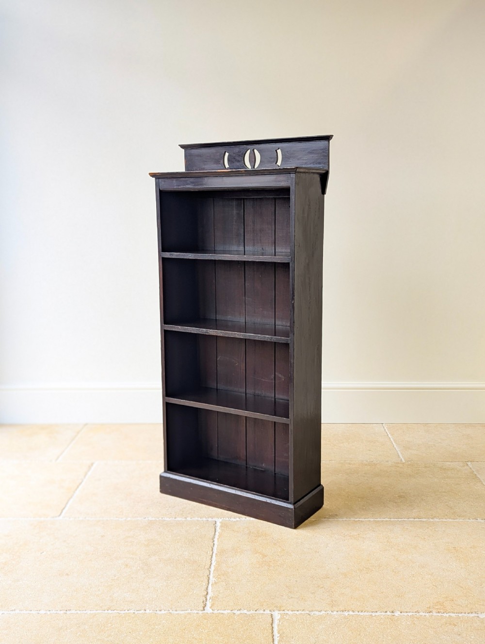 A tall, narrow late Victorian dark stained pine bookcase featuring four open shelves, a planked backboard, and a gallery top with pierced cutouts. View VII