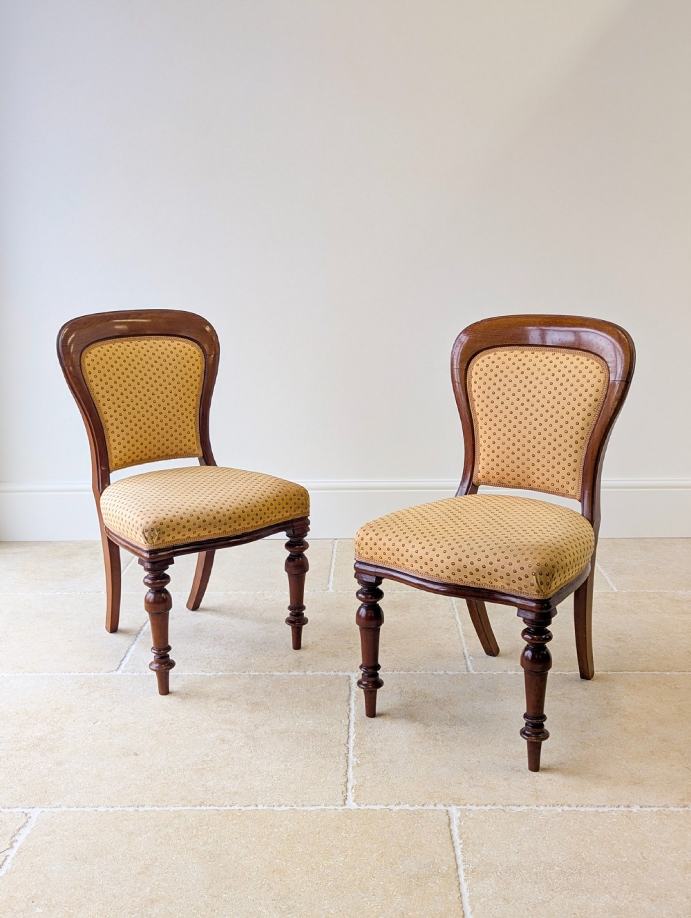 A pair of antique Victorian walnut side chairs with curved backframes, turned front legs, and patterned yellow fabric upholstery.