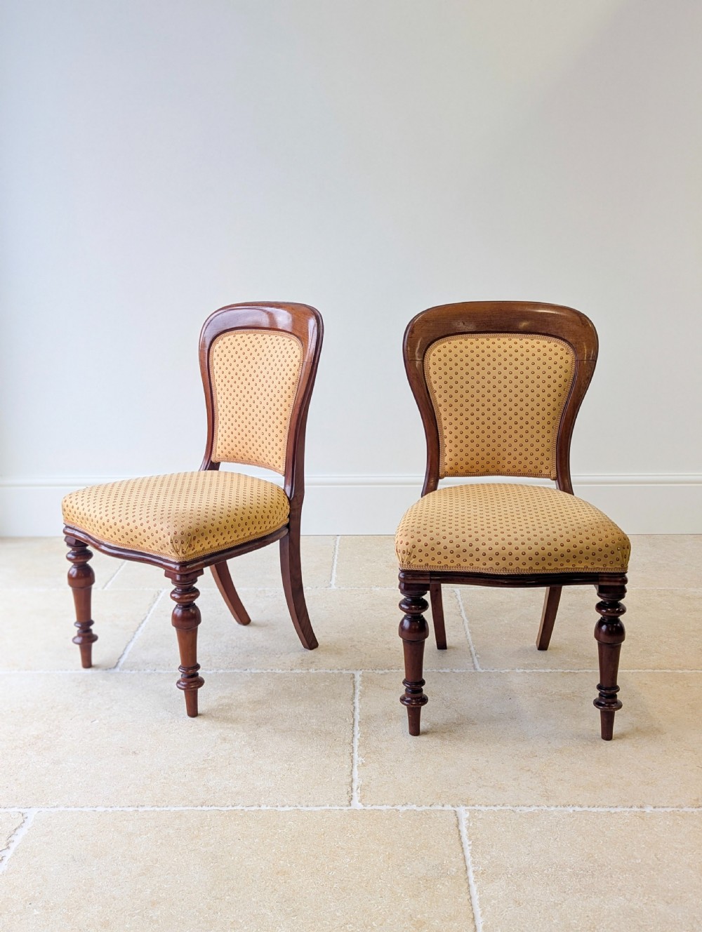 A pair of antique Victorian walnut side chairs with curved backframes, turned front legs, and patterned yellow fabric upholstery. View V