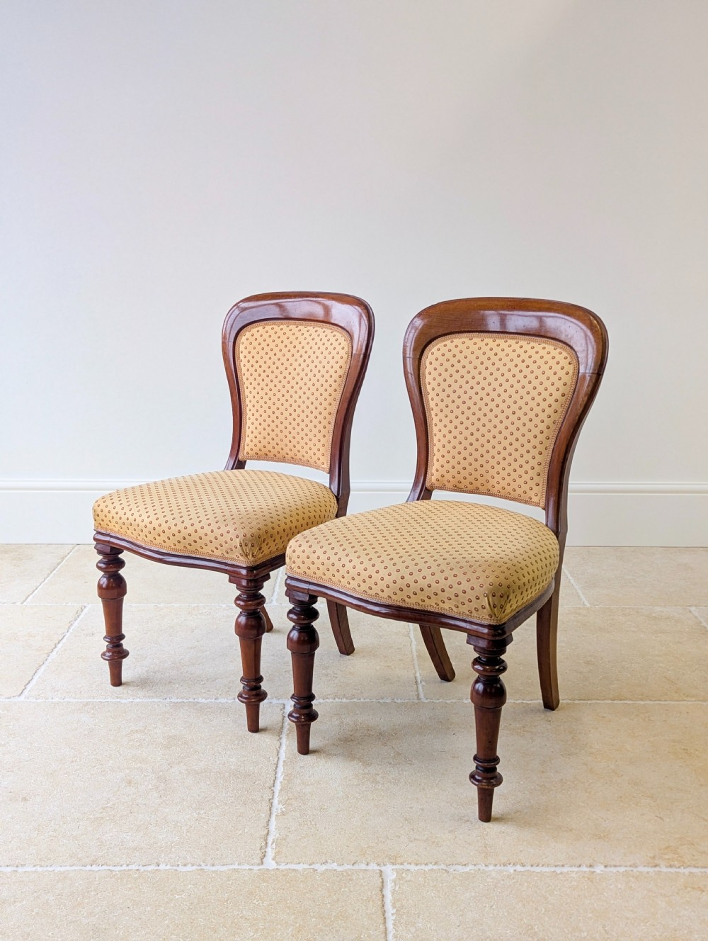 A pair of antique Victorian walnut side chairs with curved backframes, turned front legs, and patterned yellow fabric upholstery. View VI