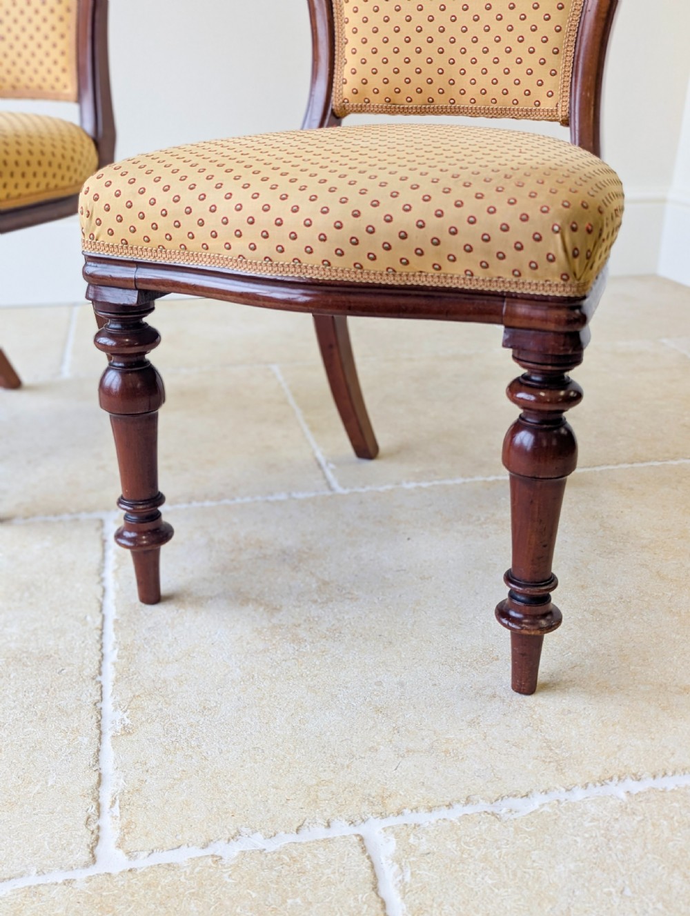 A pair of antique Victorian walnut side chairs with curved backframes, turned front legs, and patterned yellow fabric upholstery. View X