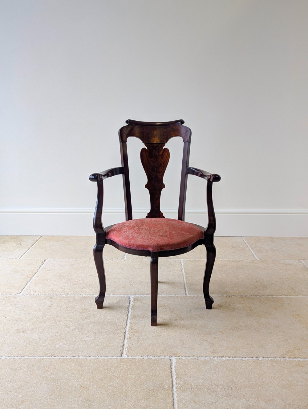 An antique mid-18th century Georgian open armchair crafted from dark mahogany wood featuring a shaped back splat, curved armrests, cabriole front legs, and a red patterned fabric seat.