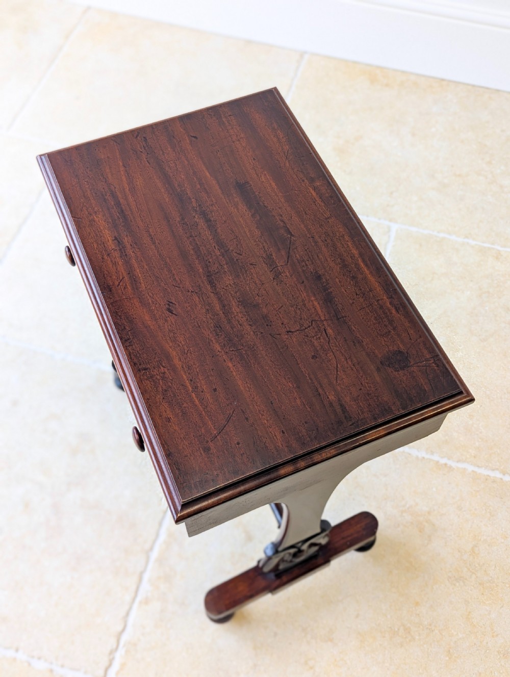 A late 19th-century Victorian mahogany sewing table featuring a top drawer with circular turned wooden handles over a deep tapered work bin, raised on scrolled lyre side supports, a turned stretcher, and castors. View II