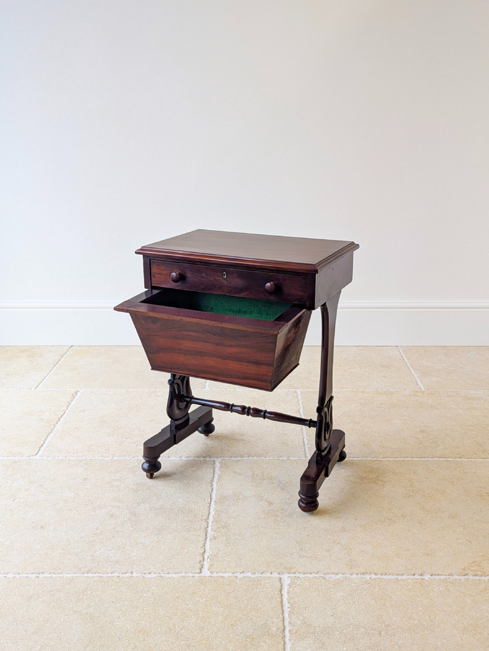 A late 19th-century Victorian mahogany sewing table featuring a top drawer with circular turned wooden handles over a deep tapered work bin, raised on scrolled lyre side supports, a turned stretcher, and castors. View III
