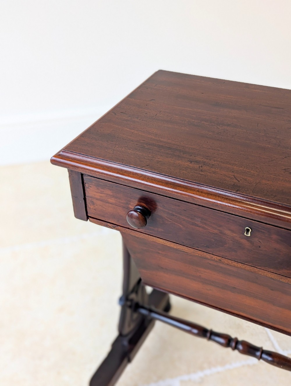 A late 19th-century Victorian mahogany sewing table featuring a top drawer with circular turned wooden handles over a deep tapered work bin, raised on scrolled lyre side supports, a turned stretcher, and castors. View V