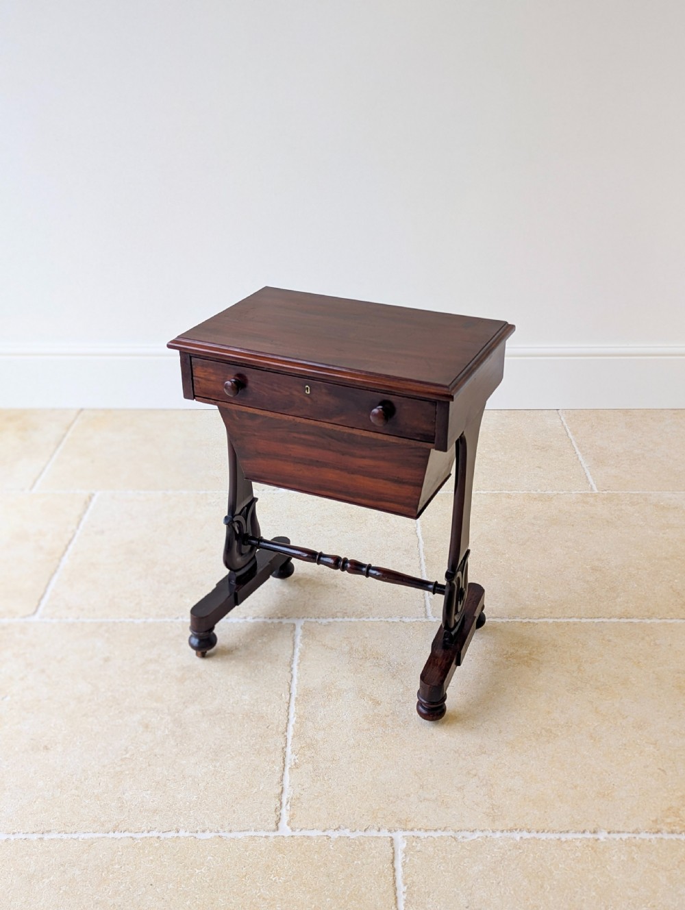A late 19th-century Victorian mahogany sewing table featuring a top drawer with circular turned wooden handles over a deep tapered work bin, raised on scrolled lyre side supports, a turned stretcher, and castors. View VIII
