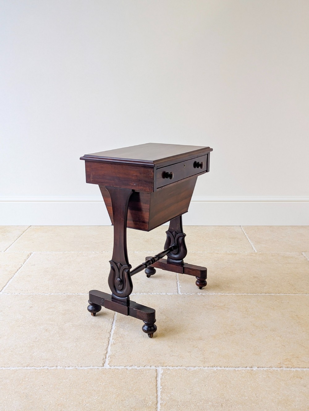 A late 19th-century Victorian mahogany sewing table featuring a top drawer with circular turned wooden handles over a deep tapered work bin, raised on scrolled lyre side supports, a turned stretcher, and castors. View X