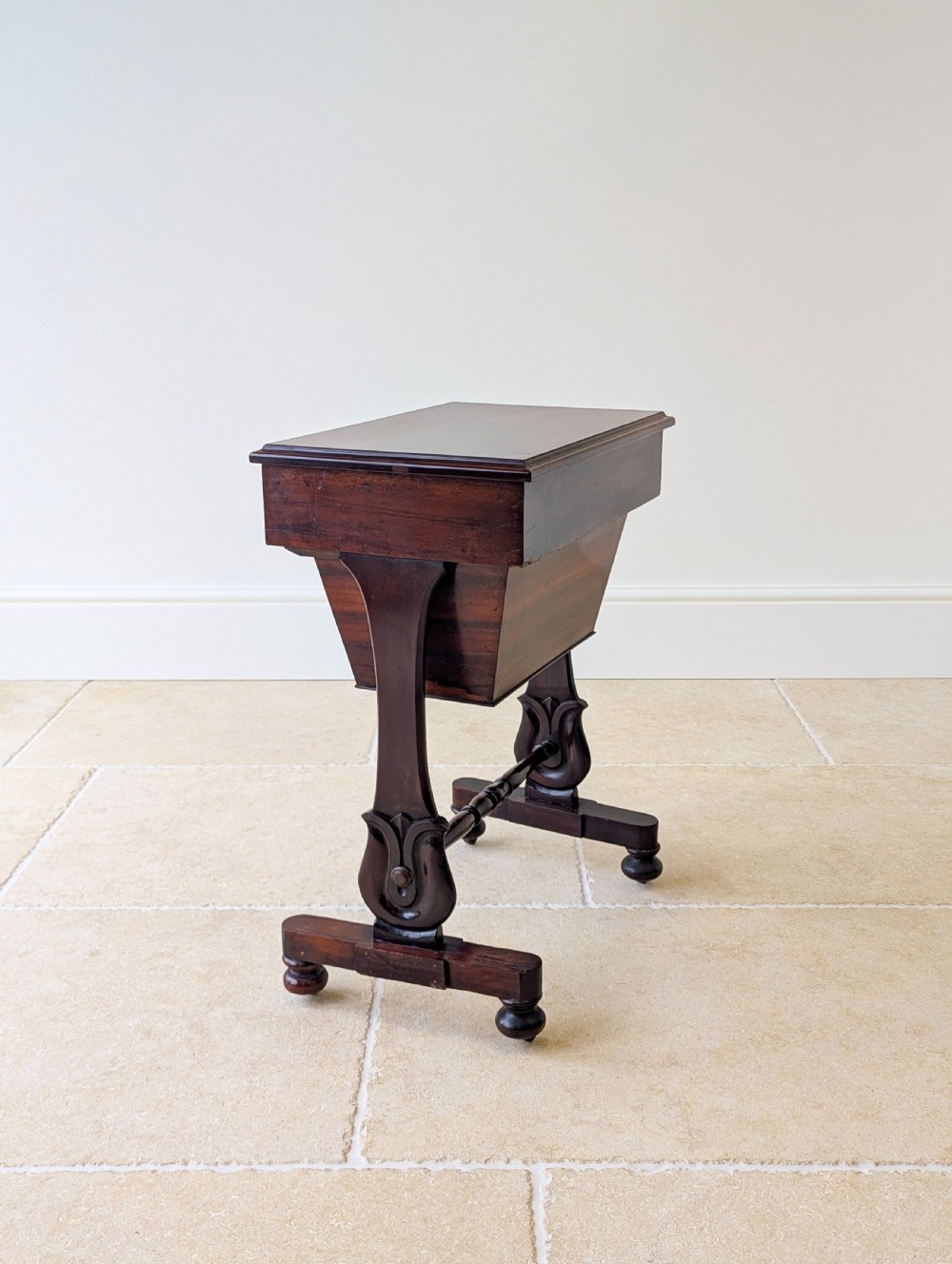A late 19th-century Victorian mahogany sewing table featuring a top drawer with circular turned wooden handles over a deep tapered work bin, raised on scrolled lyre side supports, a turned stretcher, and castors. View XIII