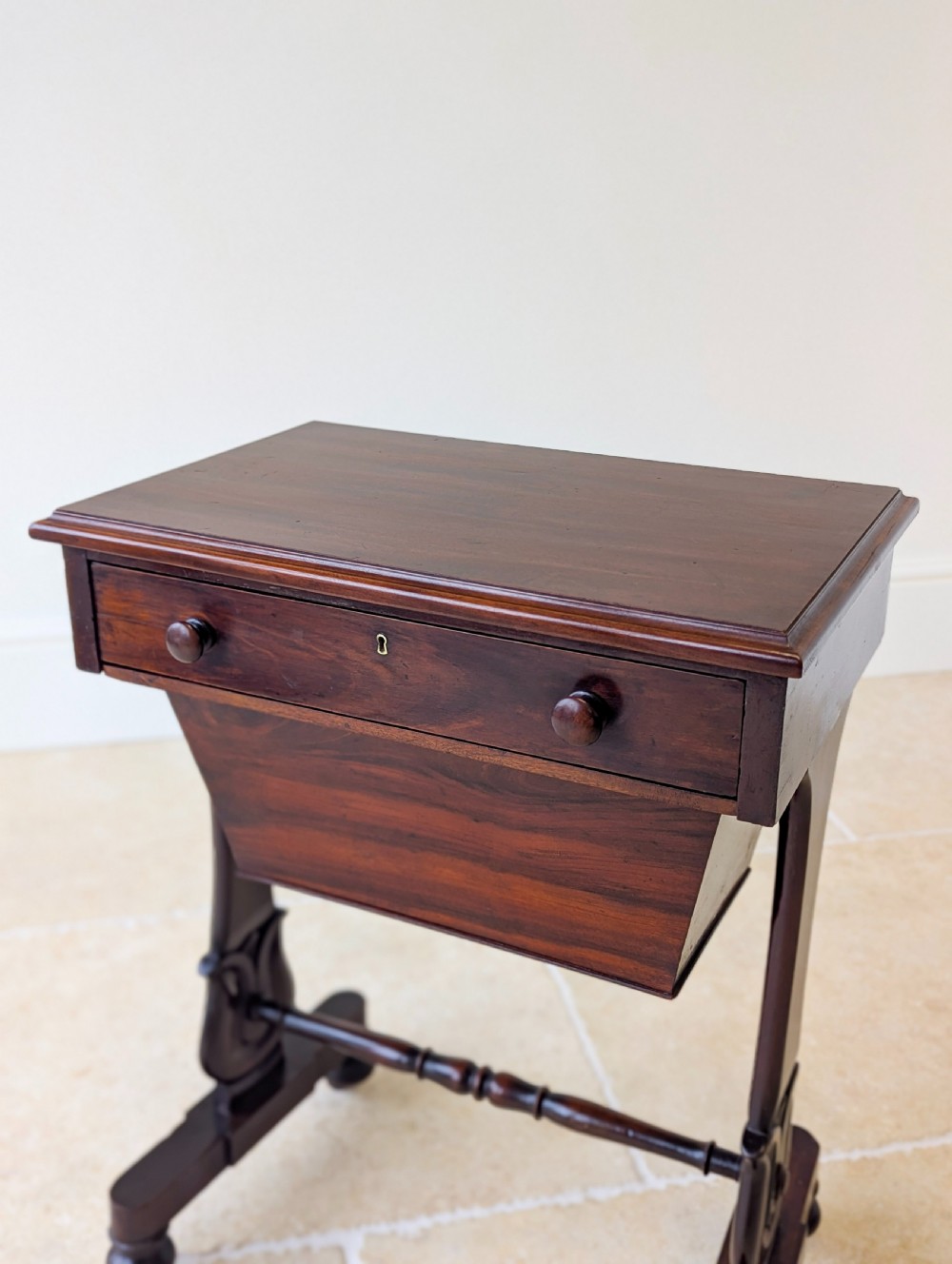 A late 19th-century Victorian mahogany sewing table featuring a top drawer with circular turned wooden handles over a deep tapered work bin, raised on scrolled lyre side supports, a turned stretcher, and castors. View XIV