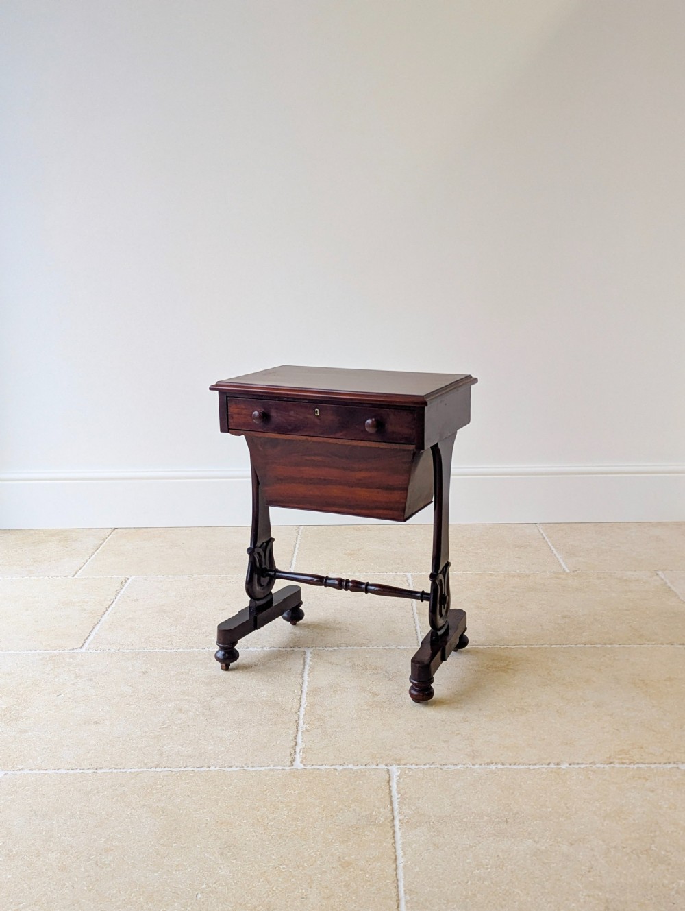 A late 19th-century Victorian mahogany sewing table featuring a top drawer with circular turned wooden handles over a deep tapered work bin, raised on scrolled lyre side supports, a turned stretcher, and castors. View XVI