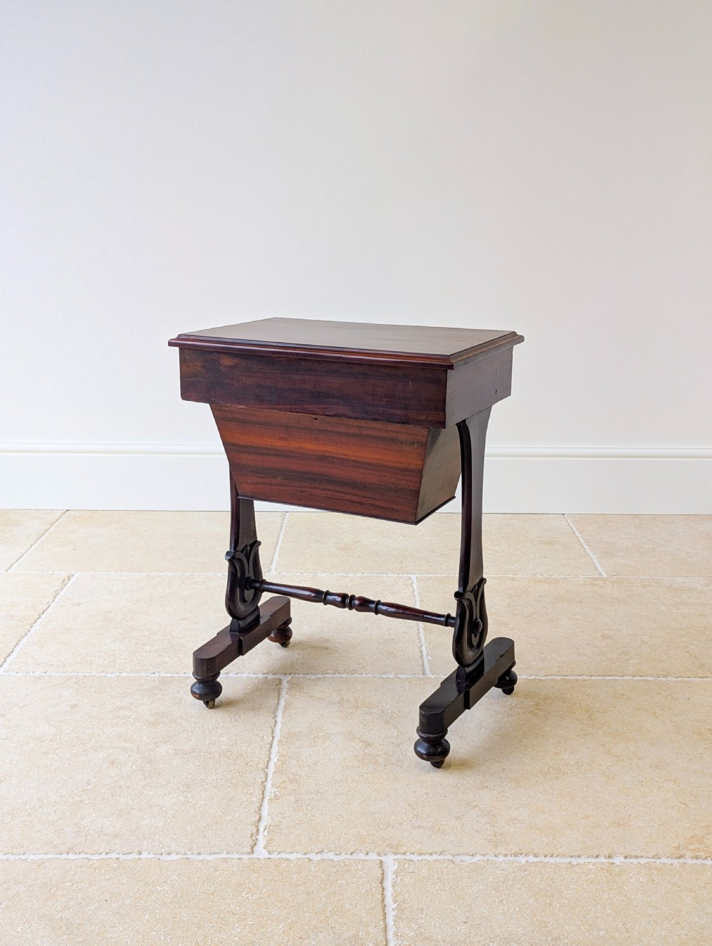 A late 19th-century Victorian mahogany sewing table featuring a top drawer with circular turned wooden handles over a deep tapered work bin, raised on scrolled lyre side supports, a turned stretcher, and castors. View XVII