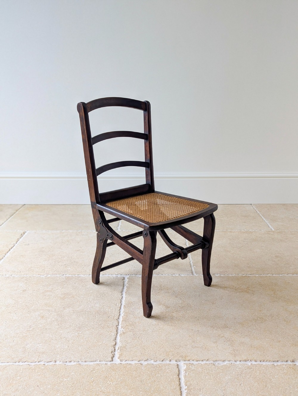 A Victorian dark wood folding campaign chair featuring a triple ladder back, a woven cane seat, and hinged folding legs. View V