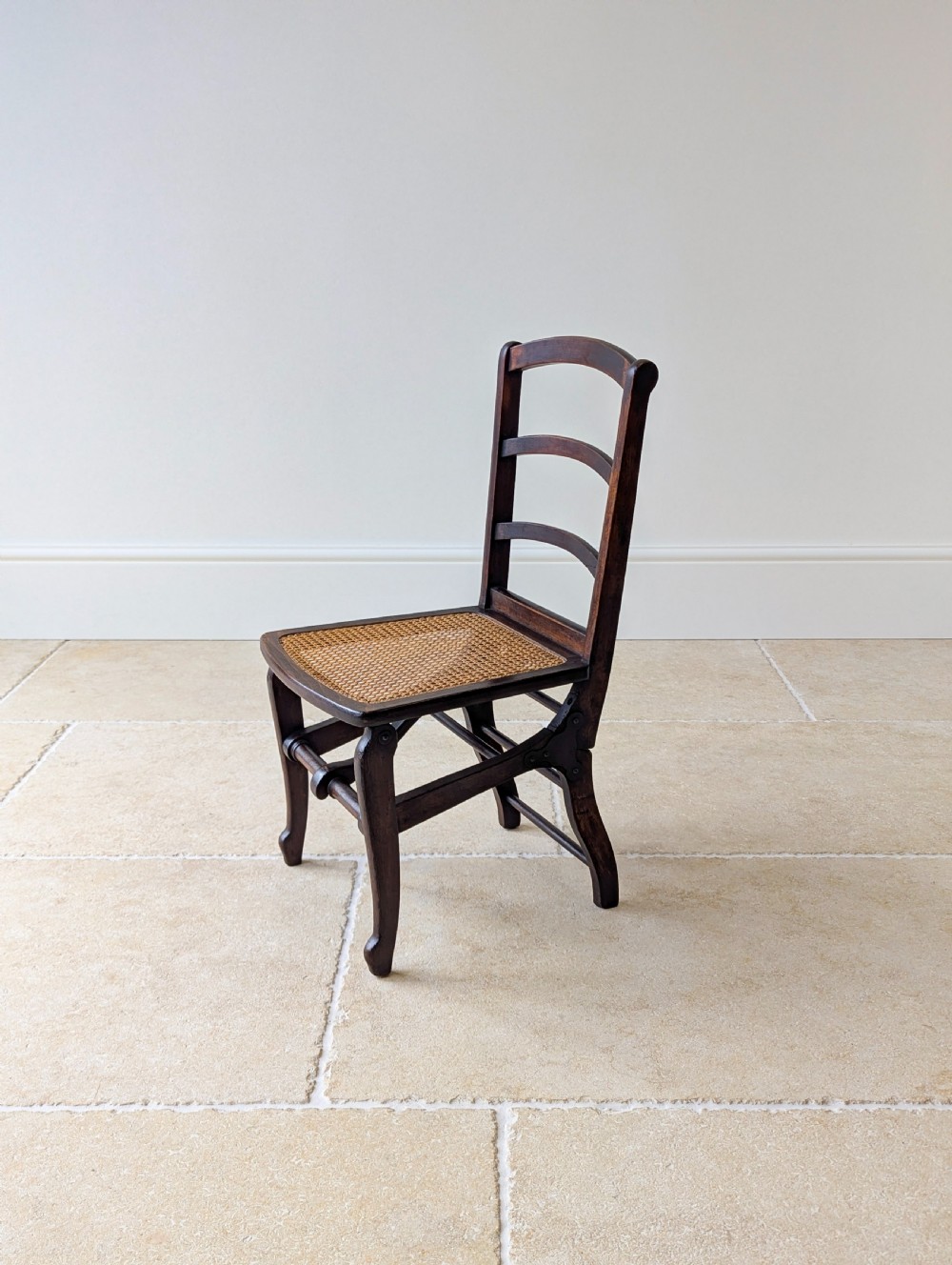 A Victorian dark wood folding campaign chair featuring a triple ladder back, a woven cane seat, and hinged folding legs. View VIII
