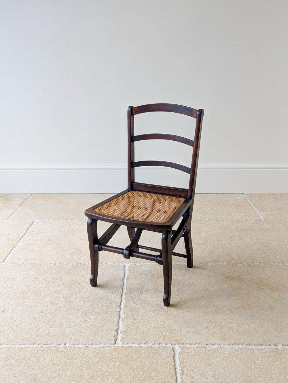 A Victorian dark wood folding campaign chair featuring a triple ladder back, a woven cane seat, and hinged folding legs. View X