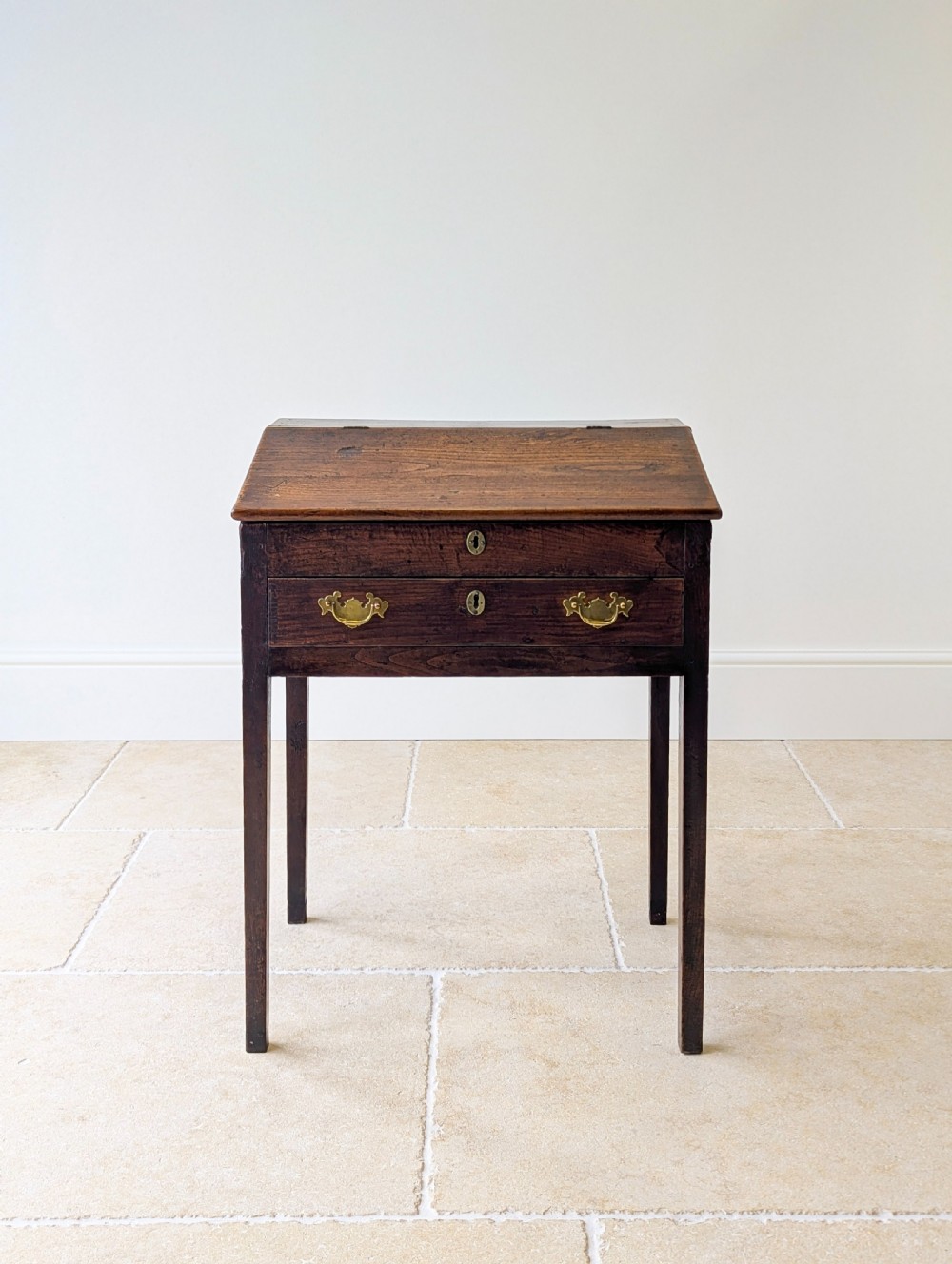 A Georgian dark elm clerks desk featuring a sloped writing surface, brass escutcheons, brass handles, and square legs. View III