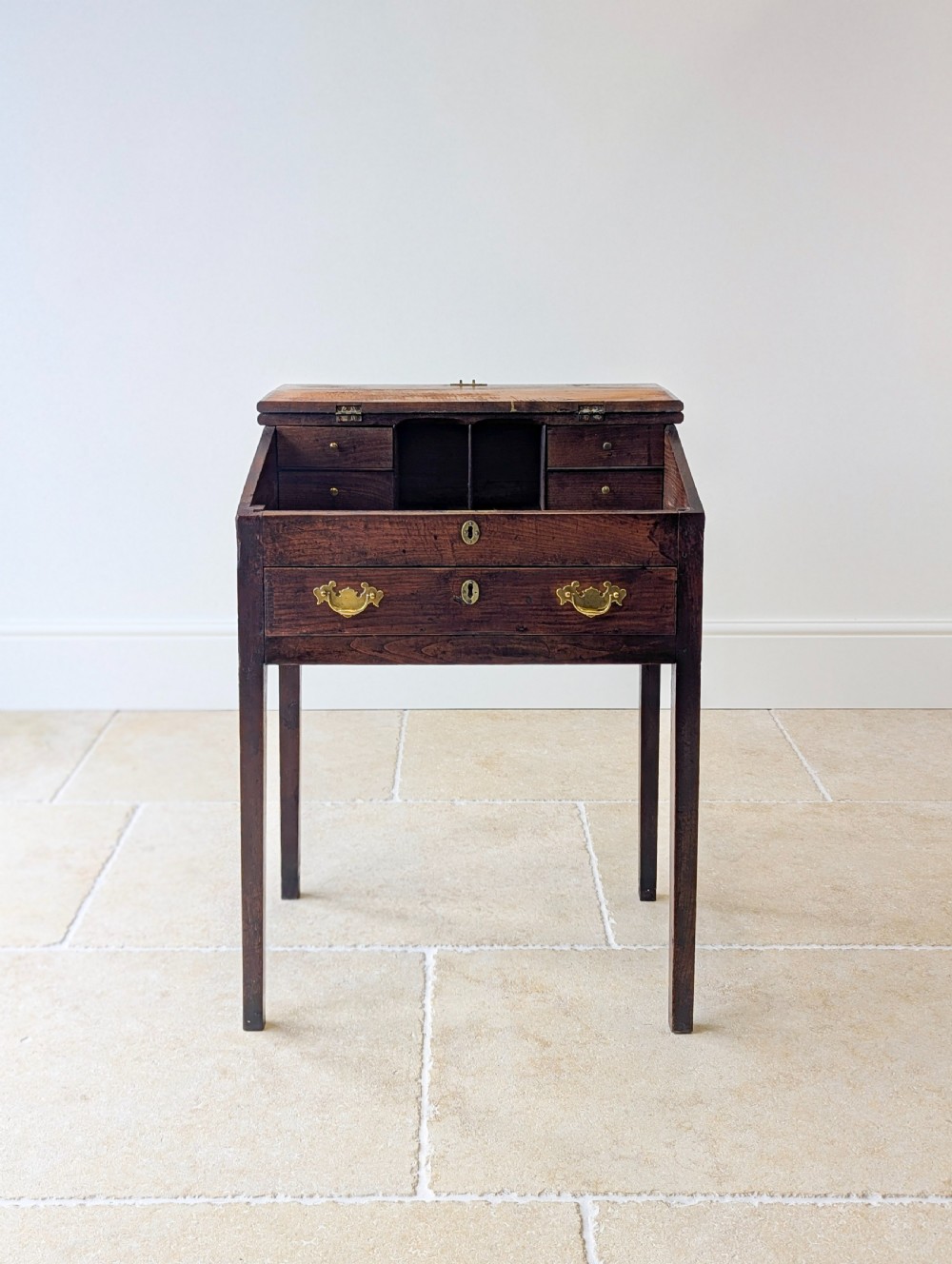 A Georgian dark elm clerks desk featuring a sloped writing surface, brass escutcheons, brass handles, and square legs. View IV