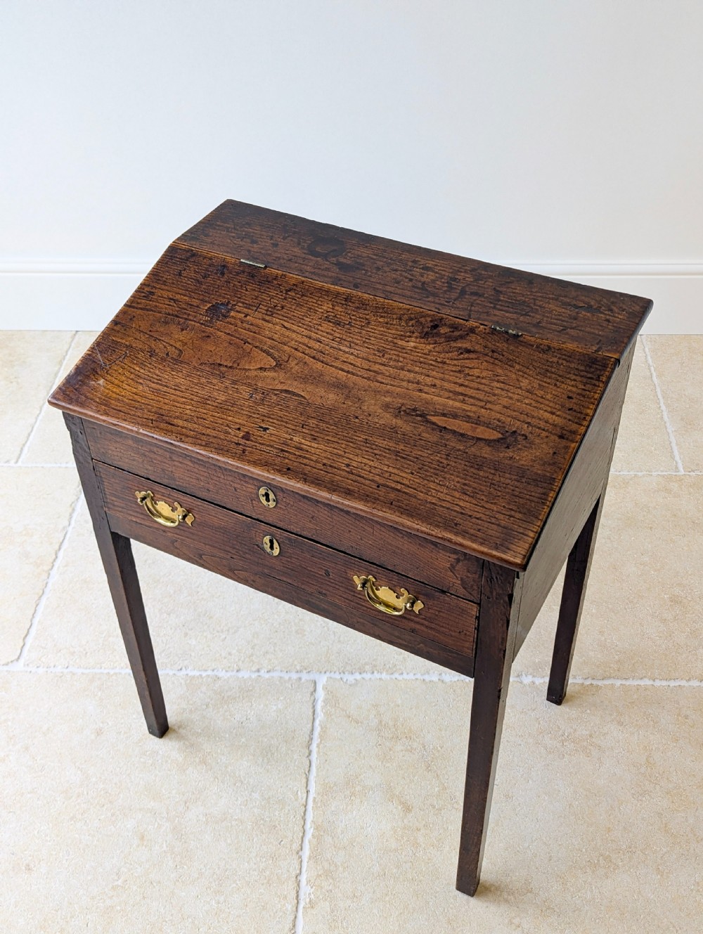 A Georgian dark elm clerks desk featuring a sloped writing surface, brass escutcheons, brass handles, and square legs. View V