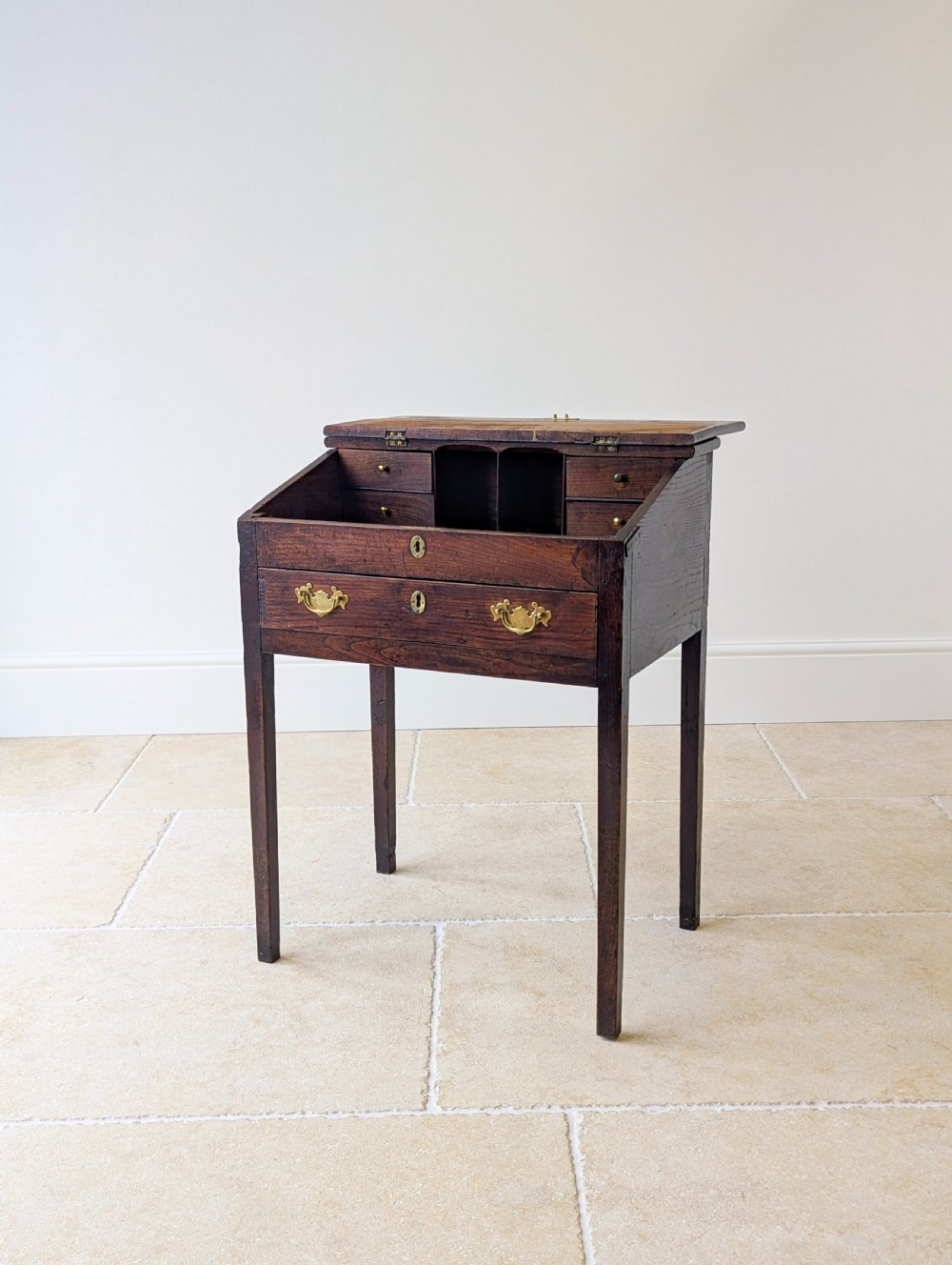 A Georgian dark elm clerks desk featuring a sloped writing surface, brass escutcheons, brass handles, and square legs. View VI