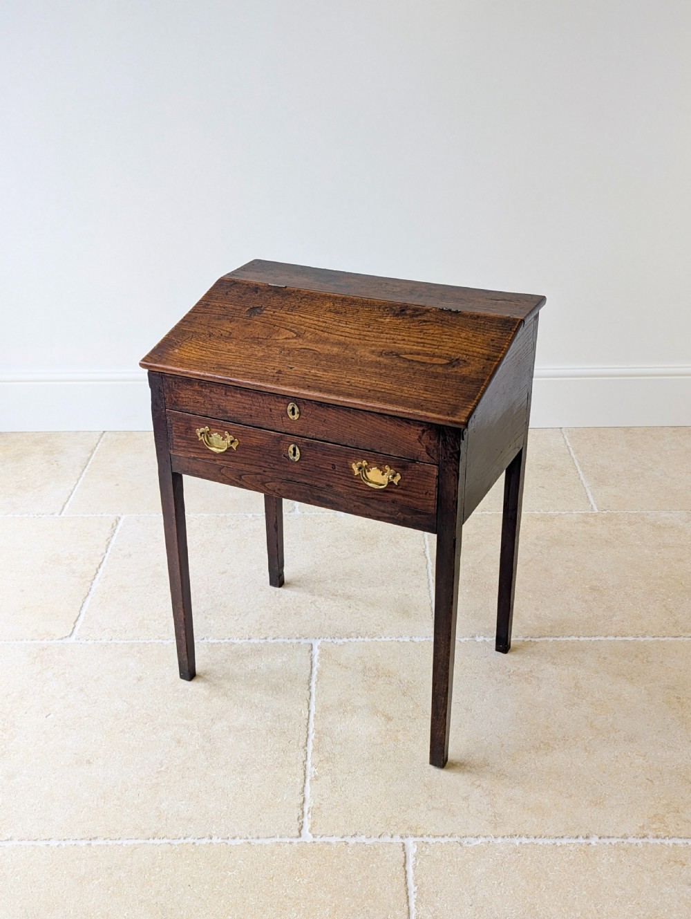 A Georgian dark elm clerks desk featuring a sloped writing surface, brass escutcheons, brass handles, and square legs. View VIII