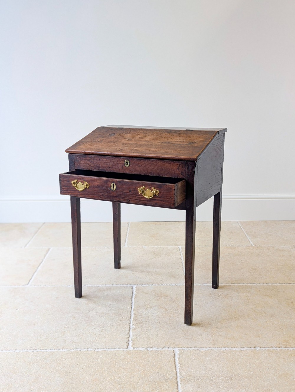 A Georgian dark elm clerks desk featuring a sloped writing surface, brass escutcheons, brass handles, and square legs. View IX