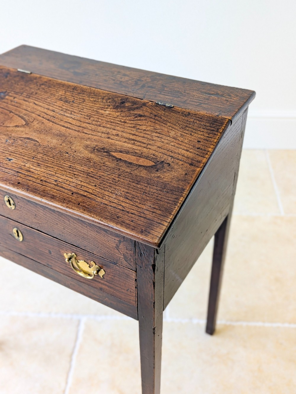 A Georgian dark elm clerks desk featuring a sloped writing surface, brass escutcheons, brass handles, and square legs. View X