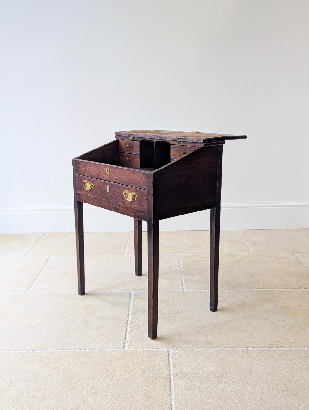 A Georgian dark elm clerks desk featuring a sloped writing surface, brass escutcheons, brass handles, and square legs. View XI