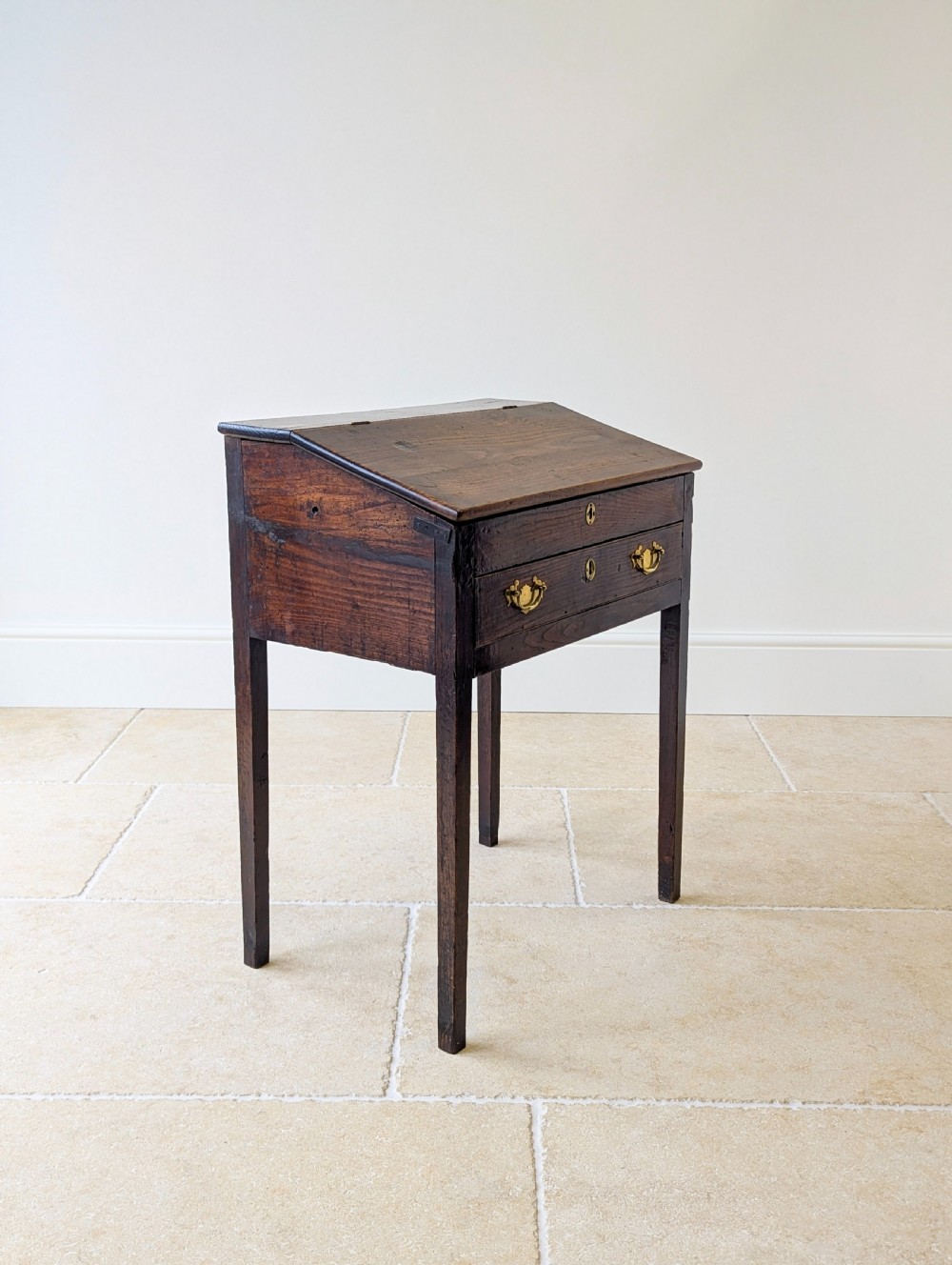 A Georgian dark elm clerks desk featuring a sloped writing surface, brass escutcheons, brass handles, and square legs. View XII